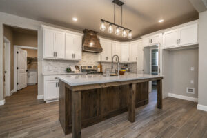 A rustic kitchen with white cabinets, a stained island and warm lighting.